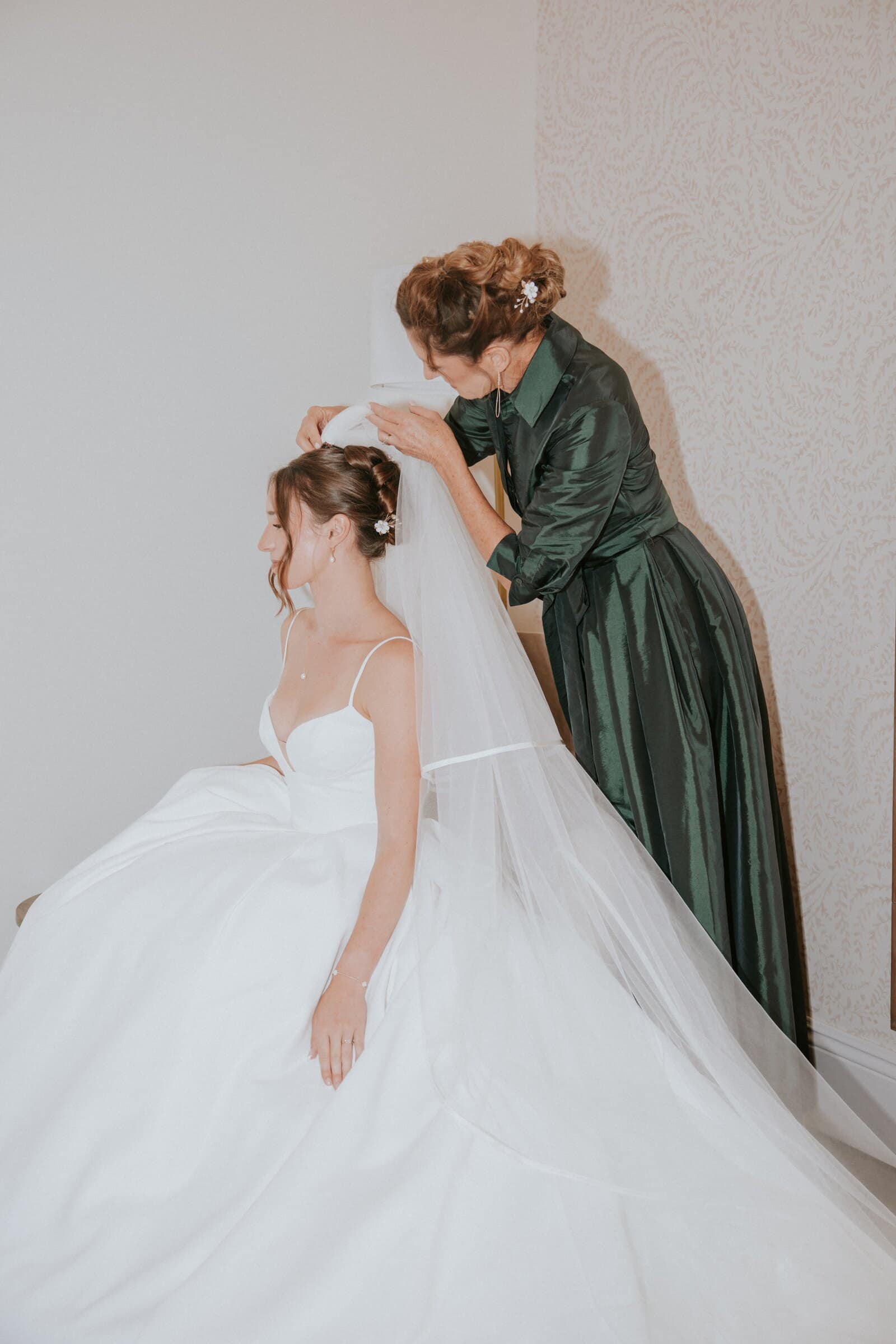 A woman in a green dress fixing Clara's veil