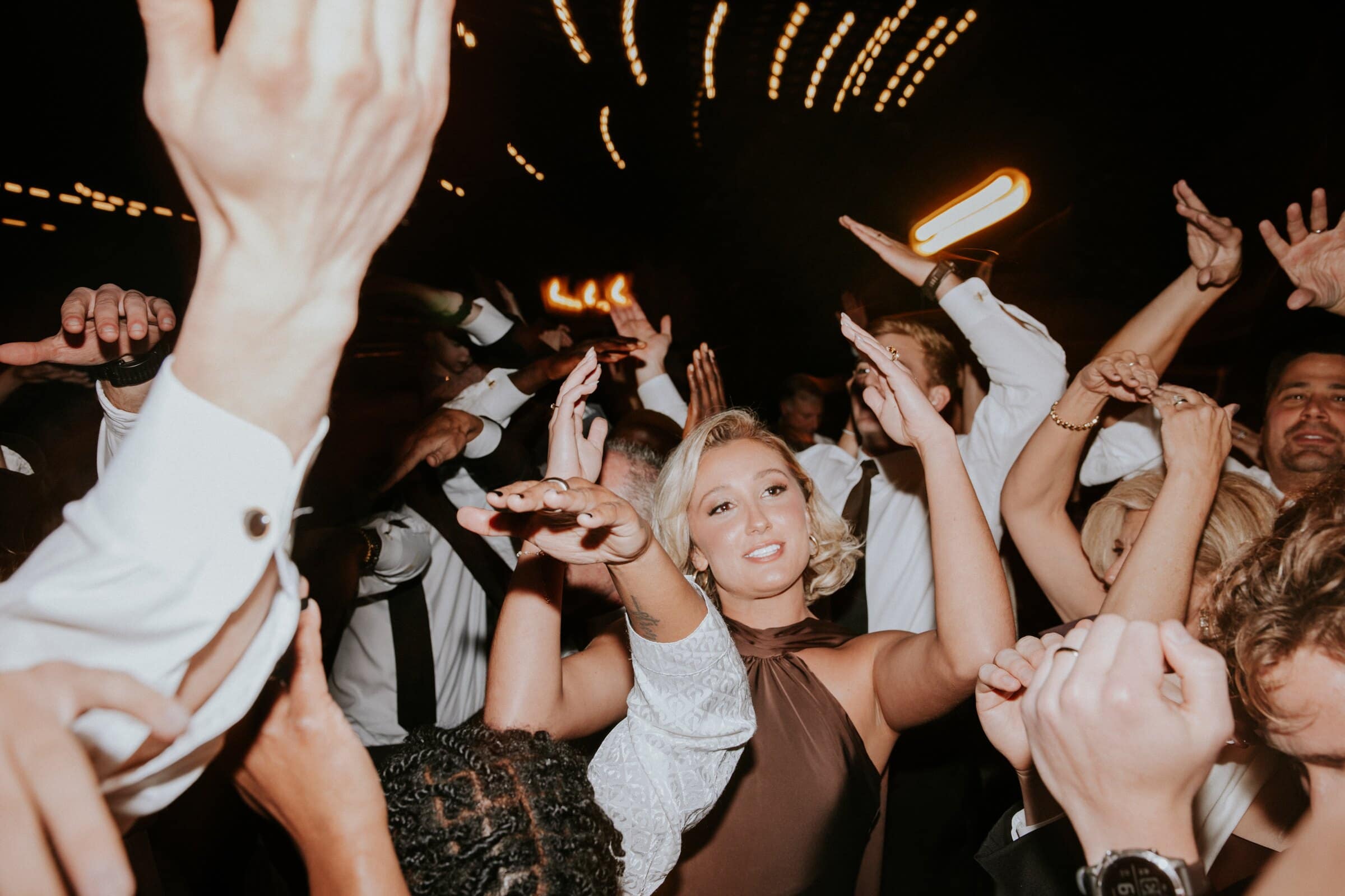 Guests throwing their hands up under streaks of string lights