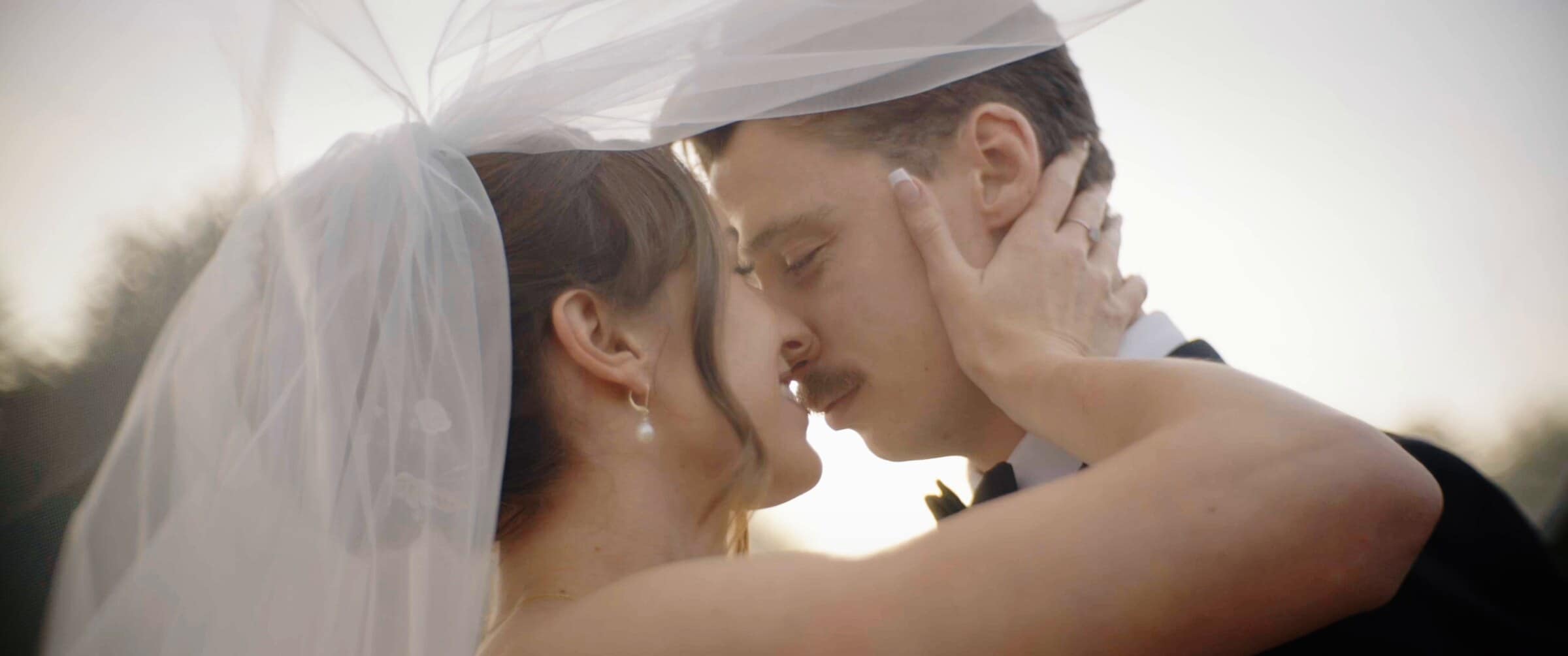 Clara and Grant kissing beneath her veil in the last of the evening light