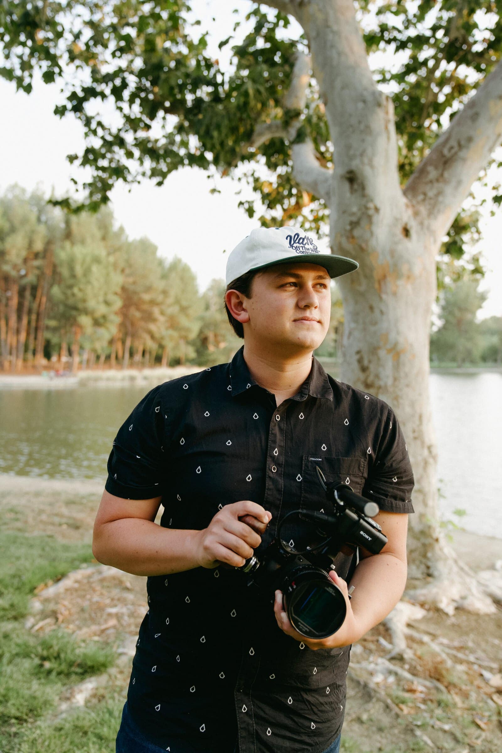 Micah Kunkle holding his cinema camera under a sycamore tree by a lake